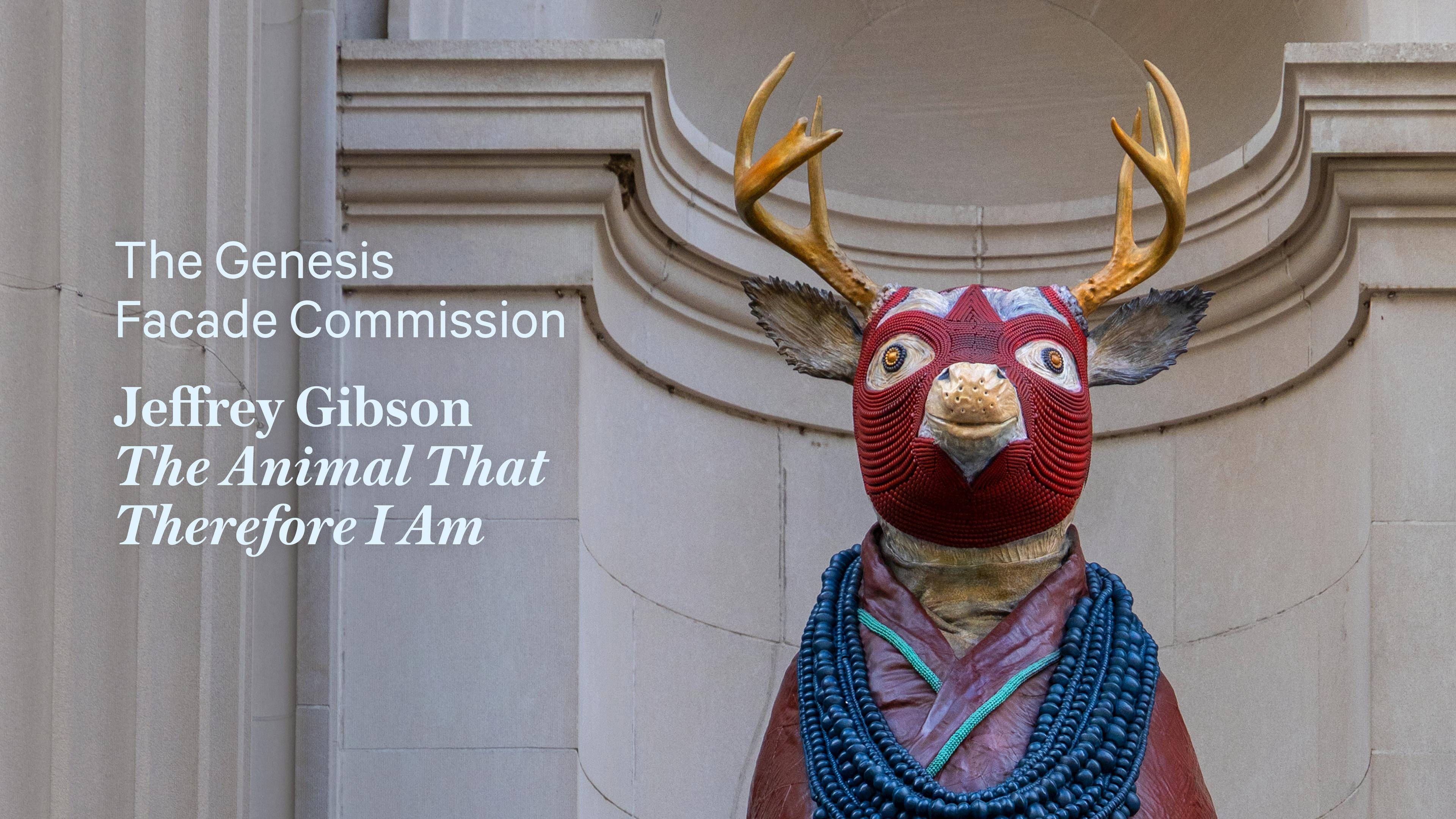 A statue of a deer with a red tribal mask and antlers stands in front of an ornate stone facade. Text reads “The Genesis Facade Commission, Jeffrey Gibson, The Animal That Therefore I Am.”