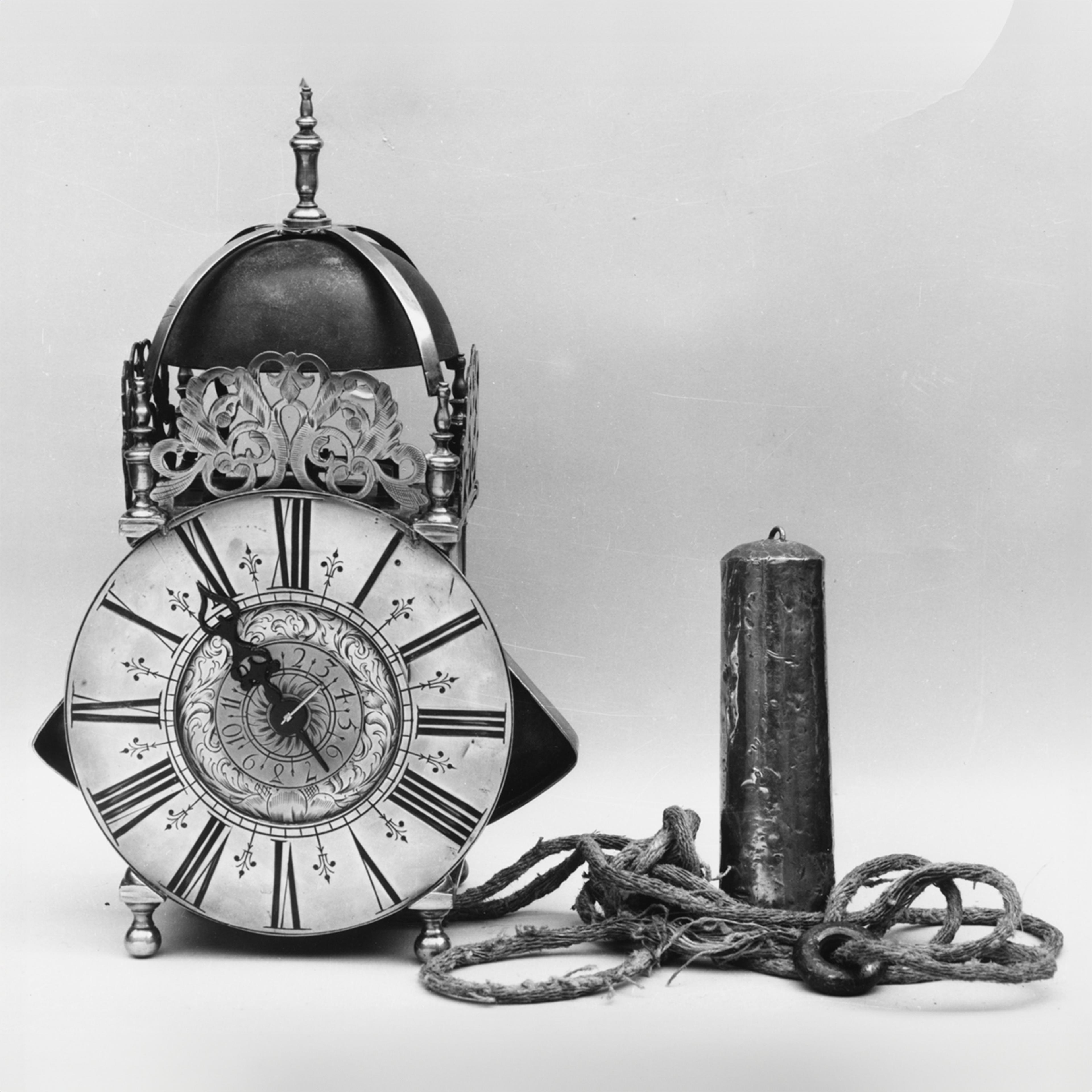 Black and white photo of a brass clock with a large face, a dome top, and a pendulum outside the clock case.