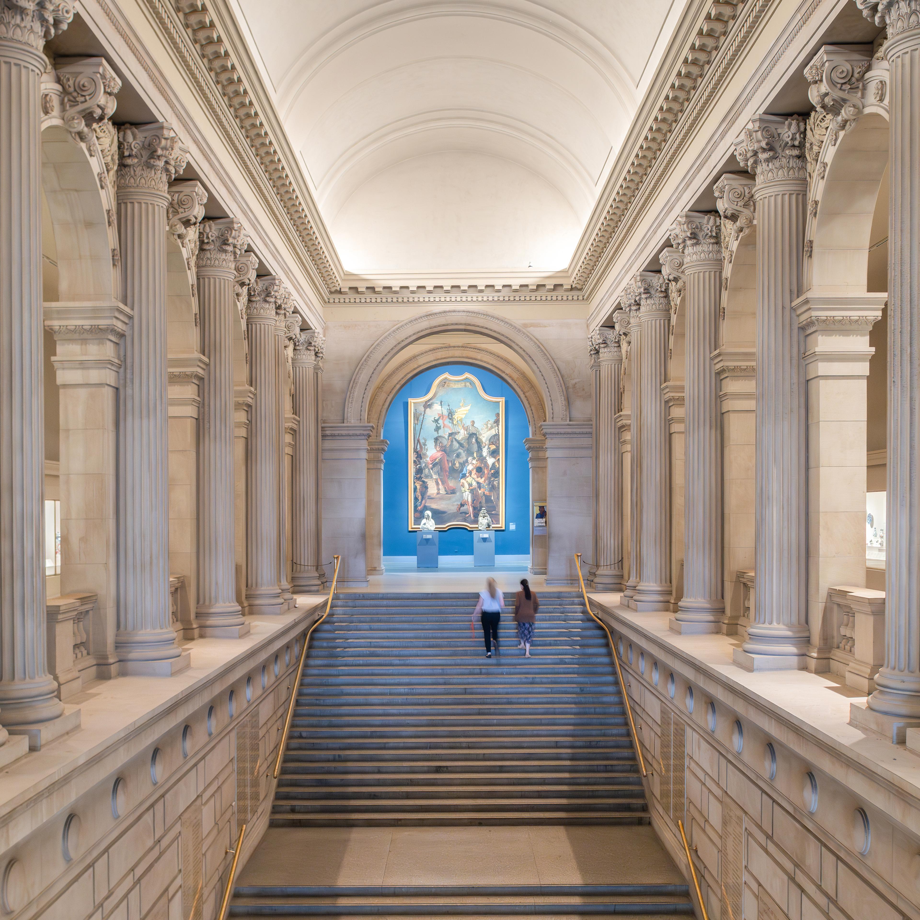 The Great Hall steps at the Metropolitan Museum of Art with two people walking up the stairs in the distance