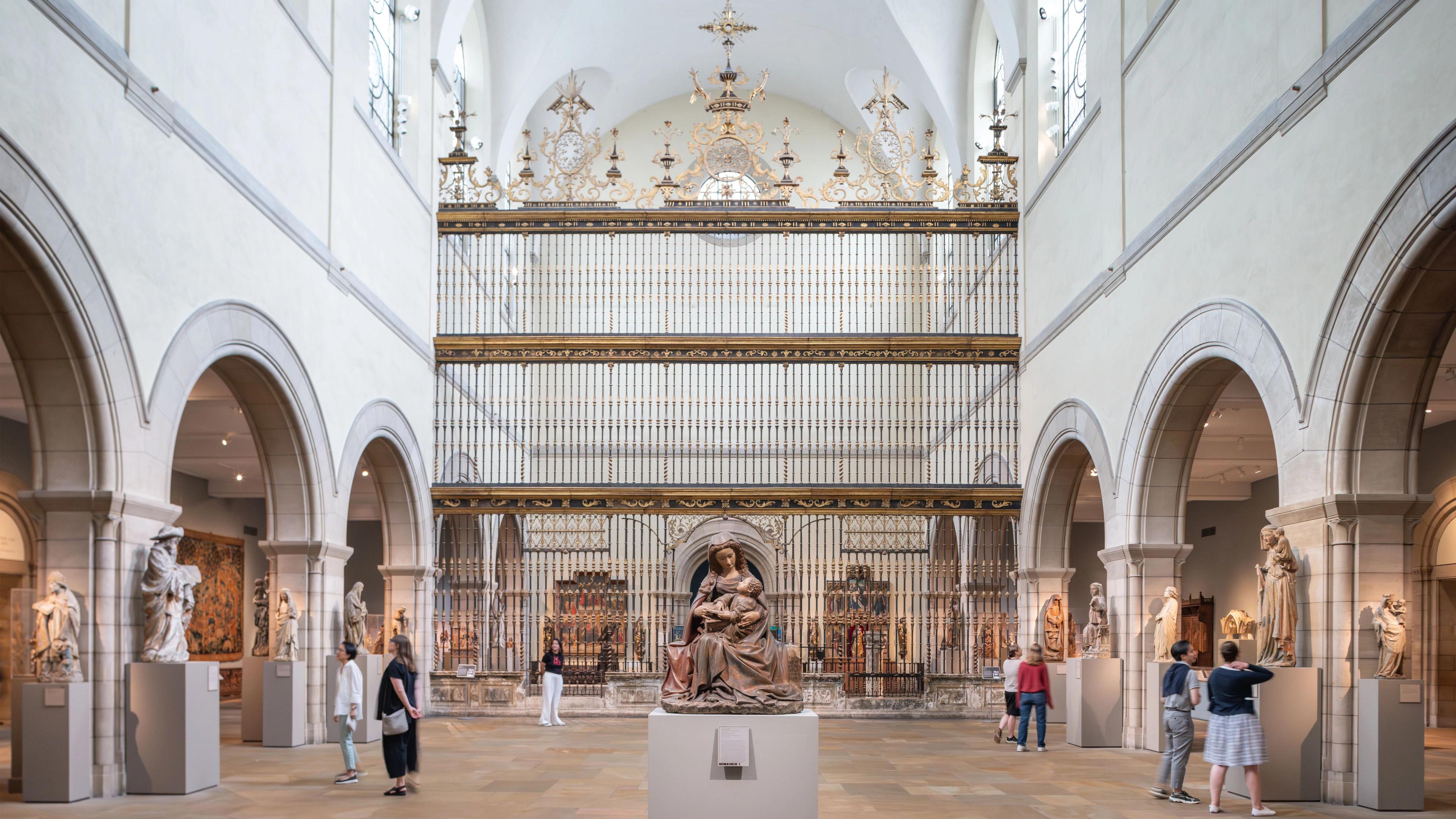 A spacious museum gallery with a Spanish choir screen in the center and filled with large-scale medieval sculptures, altarpieces, tapestries, and furniture. 