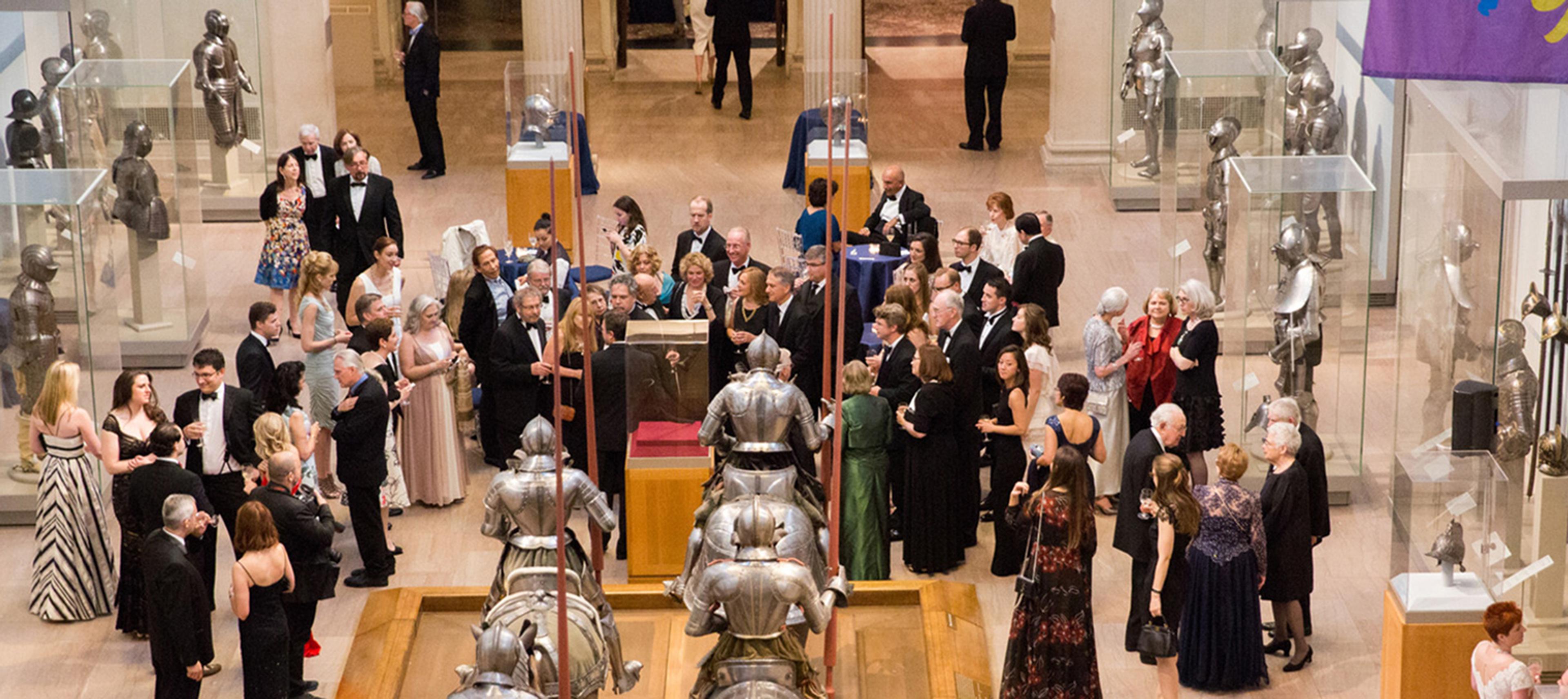 Patrons in formal wear socializing in the Arms and Armor galleries.