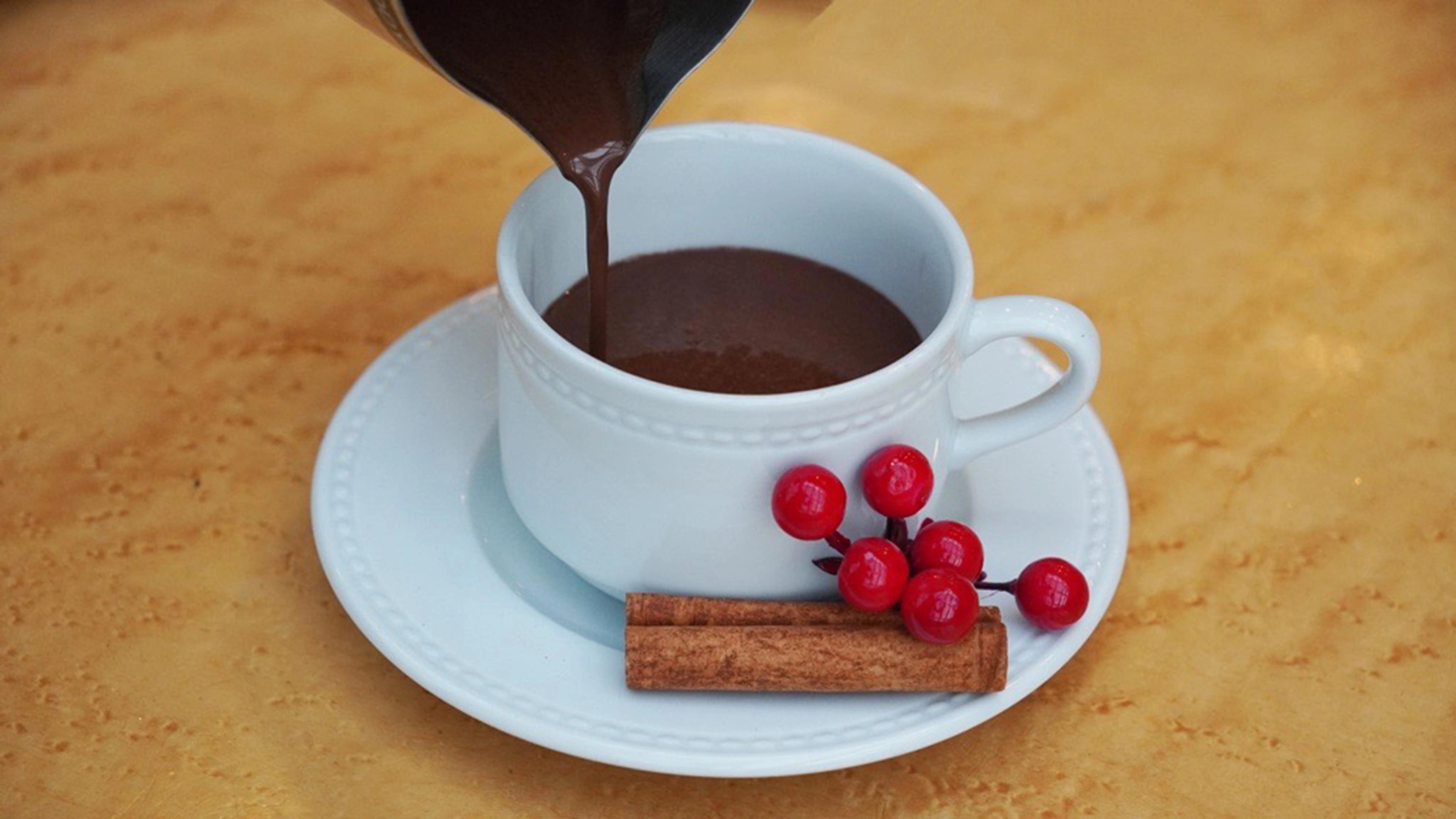 Hot chocolate being poured into a white mug placed on a white saucer.