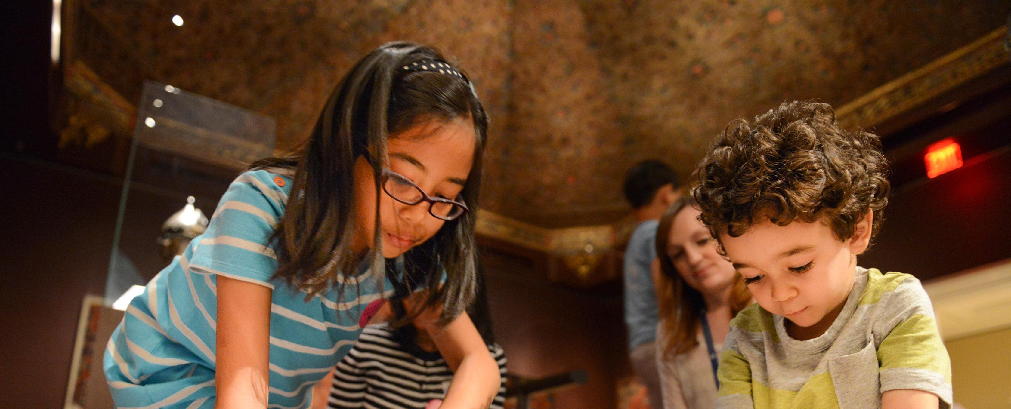 Young children in a gallery sitting on the floor with jars of shape tiles creating art.