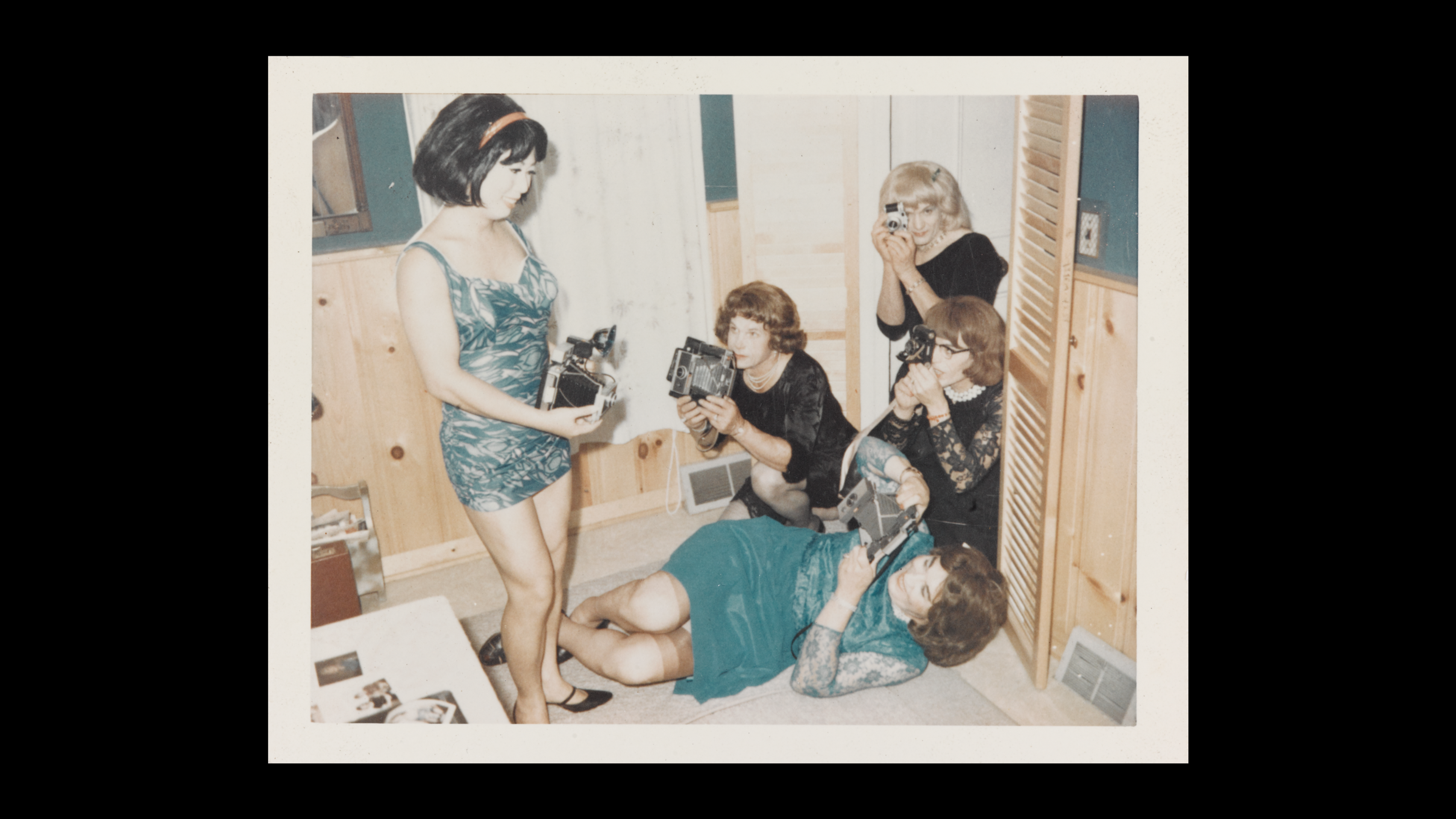 A group of women all wearing dresses, some black some green, and they all squat and stand as they take photos of one another.